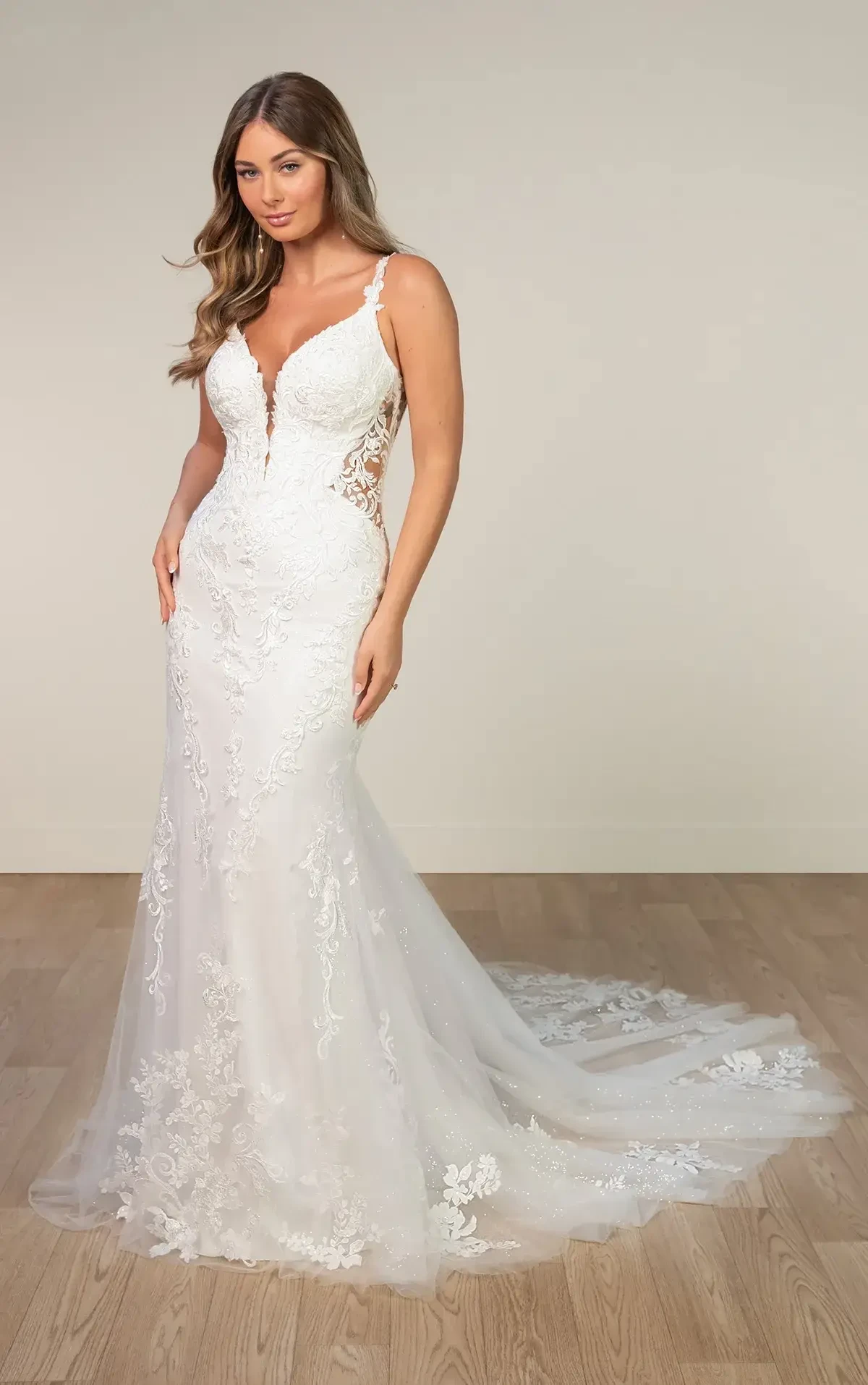 A woman in a white wedding dress with lace detailing and a fitted silhouette, standing against a neutral background.