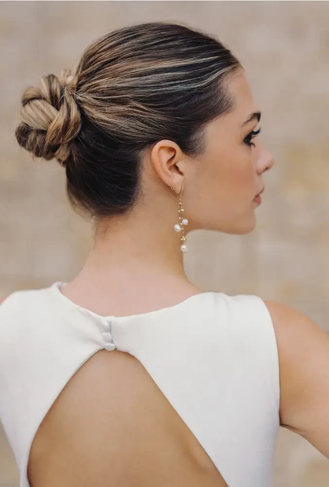 A woman with a bun hairstyle wearing a sleeveless white dress, showing her back and earrings.