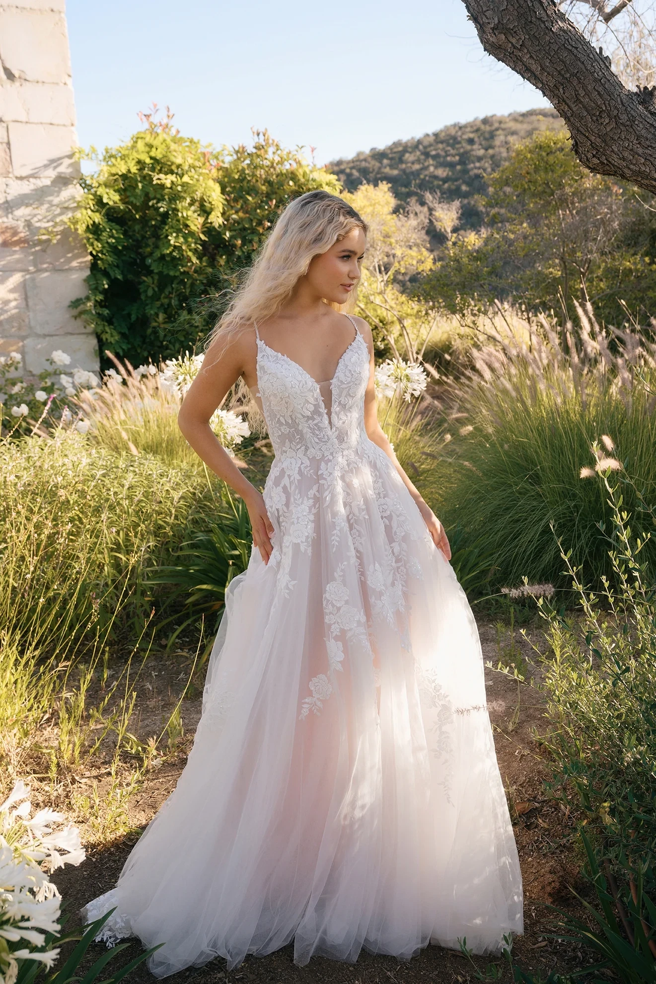 A woman wearing a beautiful white dress with intricate floral lace details, standing gracefully in an elegantly decorated room.