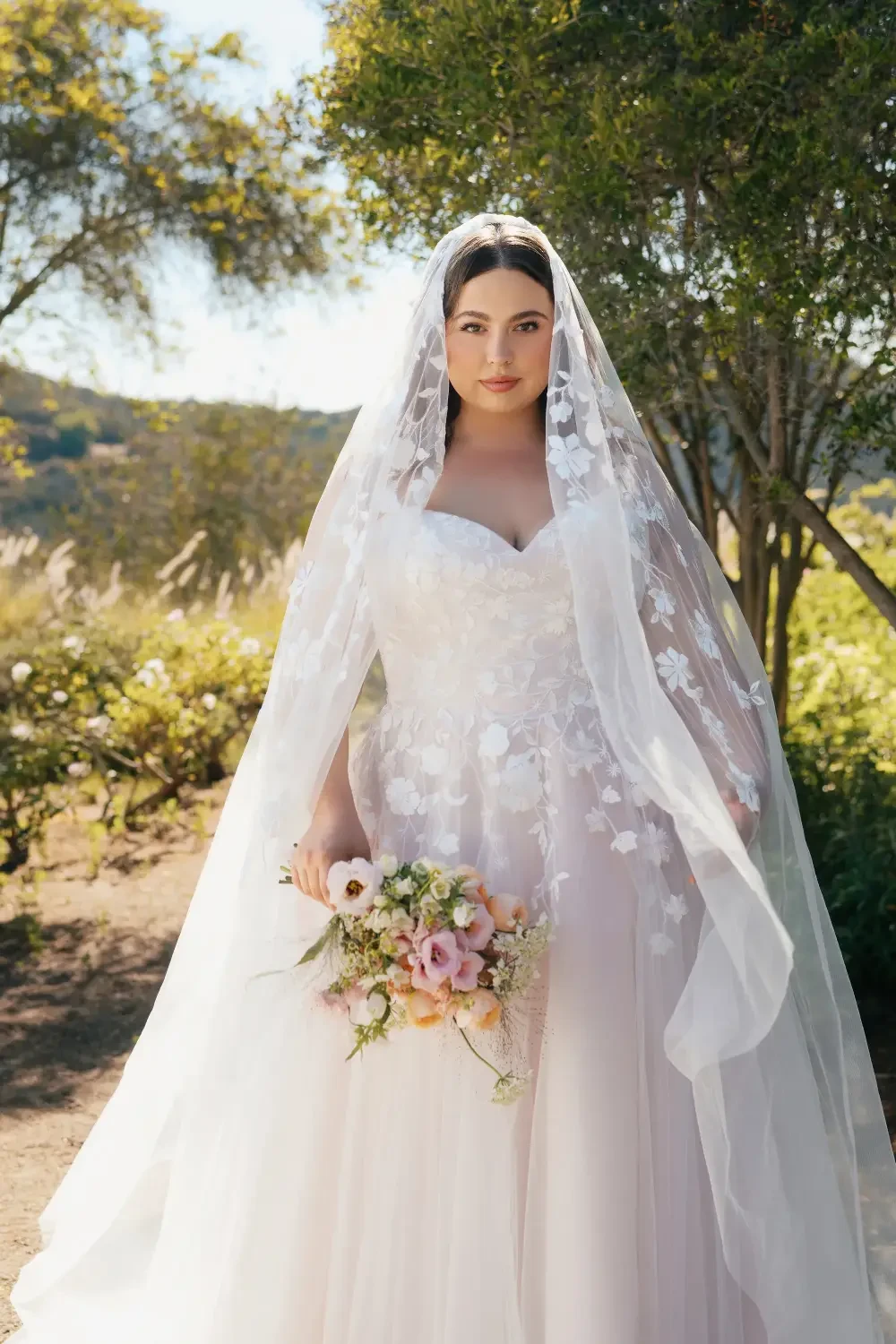 model is wearing a plus size bridal gown with a lace veil